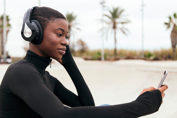 young glad ethnic female in wireless headphones surfing internet on cellphone while listening to song in city