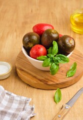 Different varieties of tomatoes in a ceramic bowl on a wooden background. Ingredients for salads.