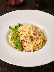 A creamy bowl of freshly made spaghetti carbonara garnished with basil leaves on a rustic wooden table