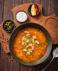 Hearty bowl of vibrant soup garnished with fresh herbs and accompanied by tangy sides on a rustic wooden table