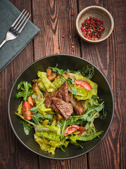 A fresh and vibrant salad featuring tender beef, crisp greens, and ripe tomatoes on a rustic wooden table