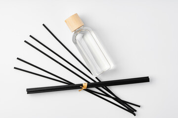 A minimalist display of essential oil and black diffuser sticks on a clean white background