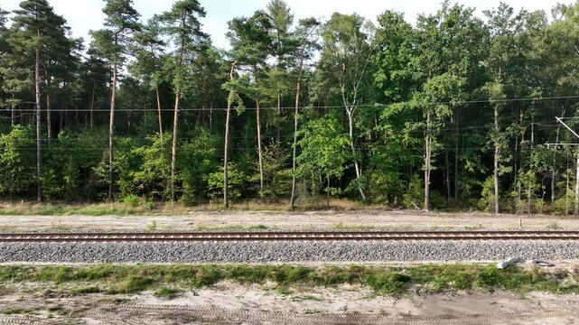 The drone shot captures a railway line set against a forest backdrop. The camera moves parallel to the tracks, providing a side view of the railway.