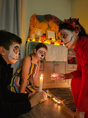 mother lights candles for day of the dead, mexican family, halloween holiday, day of the dead in mexico, skull, preparation for day of the dead holiday, masquerade, family decorates home altar for day