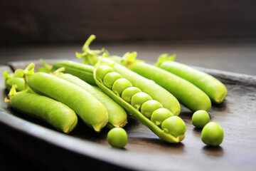 Concept, green pods of young peas, on a dark background. Social food rich in protein, fiber, minerals and vitamins. Affordable food for a healthy lifestyle. Salami goes well with legumes.