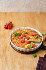 Frittata, egg casserole with cherry tomatoes, cheese and cornmeal in a light ceramic dish on a wooden background. Egg dishes.
