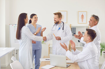 Obraz premium Happy smiling doctors shaking hands rejoicing at success in treatment standing in clinic indoors. Successful team of young medical staff in white uniform in hospital. Health care concept.
