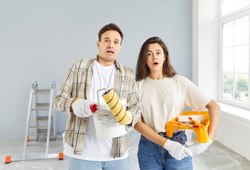 Shocked concerned young couple staring, looking, finding problems with repair in new apartment,...