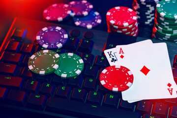 A vibrant arrangement of poker chips and playing cards on a gaming keyboard with a mouse at an online casino setup during the evening
