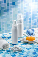  close-up captures a neat arrangement of personal care items on a tiled bathroom counter, featuring two white containers with pumps, a soft towel, a hairbrush with an orange bristle design, and a blue
