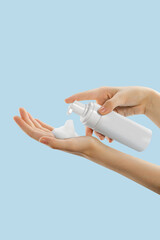 person applying a frothy skincare product from a white pump bottle into their palm against a light blue background, showcasing a skincare routine focusing on self-care and wellness. The activity empha