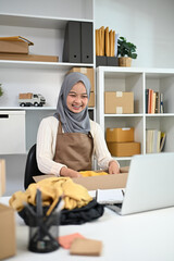 Young Muslim woman managing online store working on laptop at home office