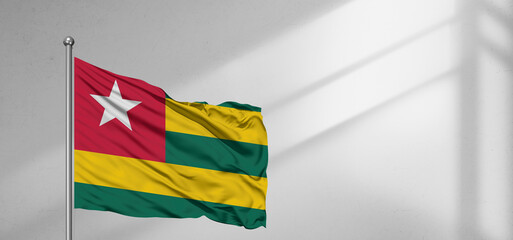 Togo national flag cloth fabric waving on beautiful window light grey Background.