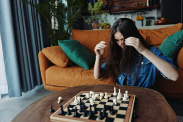 Woman sitting on couch playing chess game with hands on board in a cozy living room