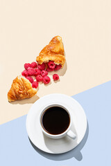 Cup of coffee and broken croissant with fresh  raspberries  on an yellow and blue background.