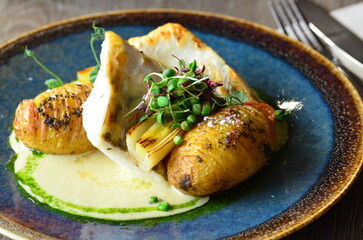 close up view of served food in restaurant on wooden table, pike perch with sauce and baked potato, herbs and micro herbs
