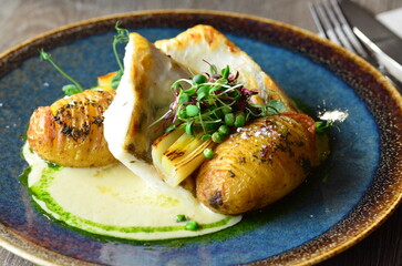 close up view of served food in restaurant on wooden table, pike perch with sauce and baked potato,...