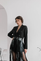 Fashion model stands gracefully with one hand on her hip, showcasing a chic black ensemble adorned...