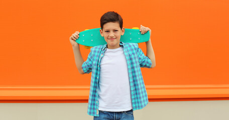 Happy teenage kid boy with skateboard in casual clothes on city street