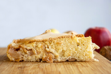 Piece of traditional thanksgiving apple cinnamon pie on the wooden cutting board on the white table, surrounded by fresh apples and walnuts. Autumn dessert. Closeup. Copy space. Top view