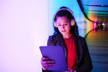 Young woman using digital tablet with headphones in neon corridor