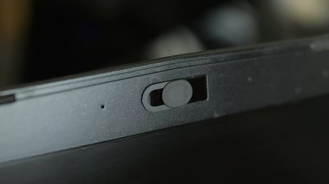 Female finger using closing webcam privacy cover slider shutter on black laptop.