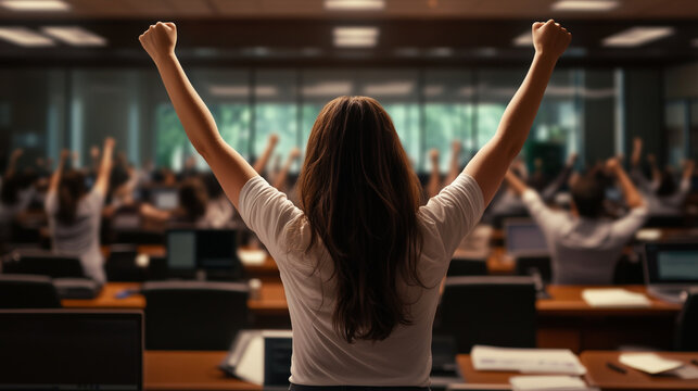 A young woman, arms raised high in jubilation, stands out in a conference room filled with employees typing on their computers, as the entire room reacts to a thrilling announcemen
