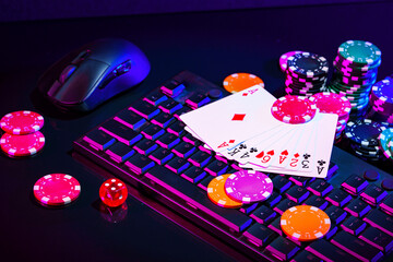 A vibrant arrangement of poker chips and playing cards on a gaming keyboard with a mouse at an online casino setup during the evening © fotofabrika