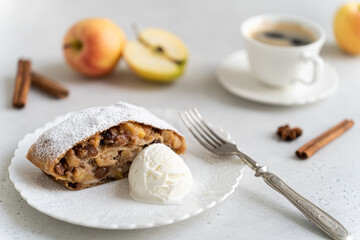 Apple pie - strudel or Apfelstrudel, sliced pie with apples, raisin, cinnamon and ice cream on white plate. Traditional German Austrian pastry. Homemade strudel with fresh apples and powdered sugar