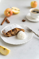 Freshly baked powdered apple strudel with raisins and ice cream on white plate with red apples and cinnamon on white background. homemade Apfelstrudel, austrian germany cuisine. Menu, recipe, close up