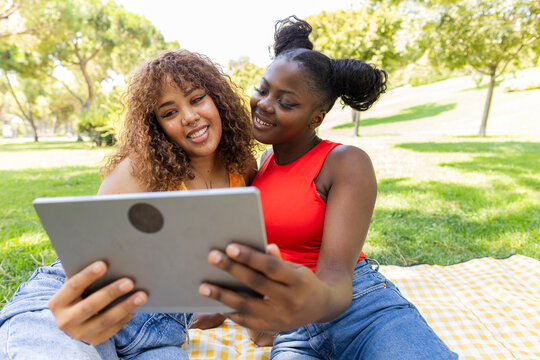 Two diverse LGBTQIA+ women enjoying time in the park with a tablet - Powered by Adobe