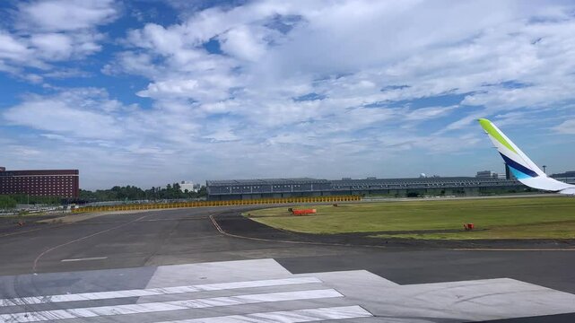 Airplane wing view while taxiing on a runway at a large international airport under a cloudy sky
