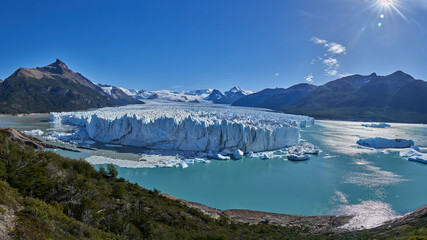 Fototapeta premium Perito Moreno Glacier in Patagonia, Argentina, captured at noon. The bright sunlight illuminates the vast expanse of ice, highlighting its majestic beauty against the clear blue sky.