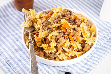 Easy homemade pasta with minced meat. One pot pasta with ground beef and autumn vegetables, in portioned plate on kitchen table