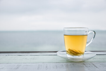 Cup of green tea with ginger  front of at sunset light on wooden tabletop. Sea view.