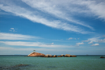 Fototapeta premium Big rock on the seashore front of the small tropical rock island with lone tree. Ocean view.