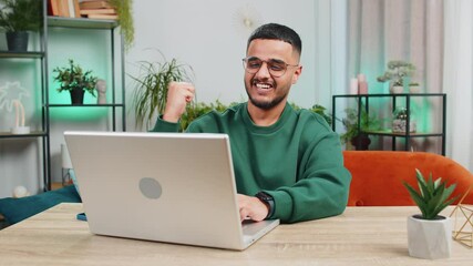 Surprised Indian young man using laptop computer, receive mail good news message shocked by sudden victory celebrate lottery jackpot win purchases online shopping play game at home apartment at table