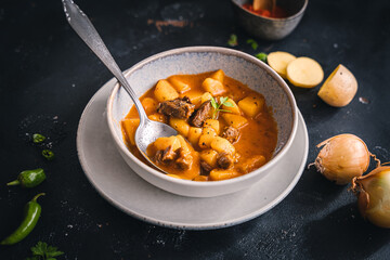 Gulaschsuppe mit Kartoffeln in einer Schüssel auf einem schwarzen Tisch. Abendessen, servierfertig.