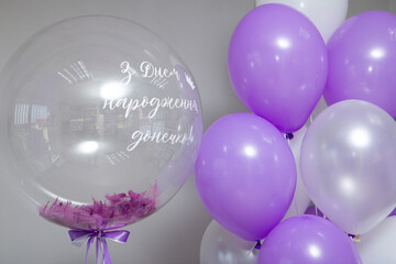 a transparent bubble balloon with purple feathers and a bunch of helium balloons, the inscription: "Happy birthday, daughter!"