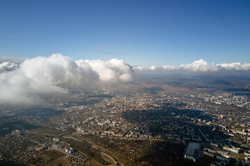 Aerial view from airplane window at high altitude of distant city covered with white puffy cumulus clouds