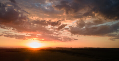 Bright colorful sunset sky with setting sun and vibrant clouds over dark landscape