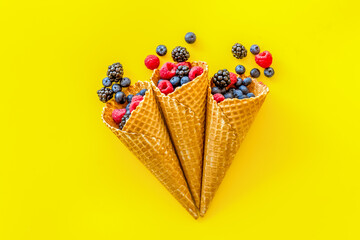 Summer breakfast with fresh berries in waffle cones on yellow ba