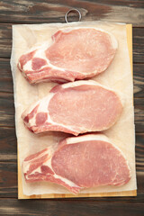 Sliced raw pork meat on cutting board on brown wooden background. Vertical photo