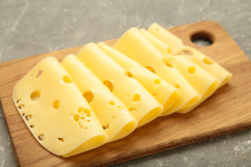 Cheese slices on cutting board on grey background.