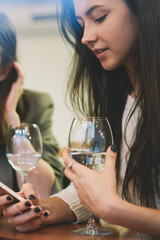 Caucasian millennial women socialising online and ignoring live communication during wine time with friends, beautiful hipster girls chatting online via modern cellular gadgets connected to wireless