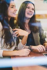 Happy caucasian female friends feeling excited during leisure time togetherness for drinking wine in cafe interior, positive smiling women sitting at cafeteria table and posing for selfie with glasses