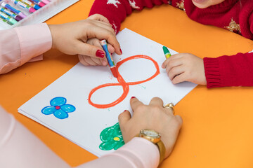 Close up shot of cute girl writing numbers on the paper learning how to calculate numbers in math sitting on chair beside assistant teacher in classroom at school, Learning for kids concept