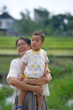 A middle-aged woman carrying her son walking around the rice fields