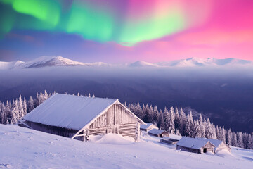 Old wooden cabins in snowy mountains under incredible Northern lights in starry sky. Christmas...