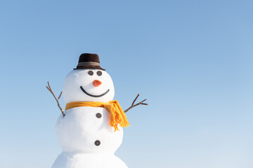Funny snowman in stylish brown hat and yellow scard. Clear Blue sky on background